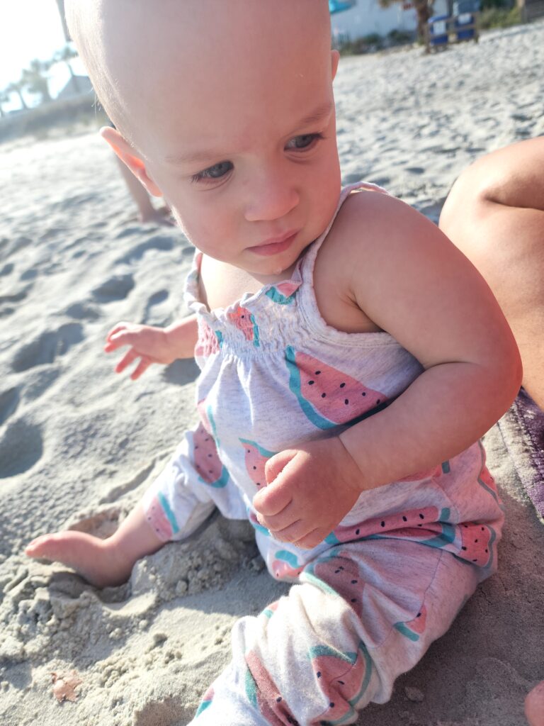 Toddler girl sitting in the sand allowing her to explore her senses. 